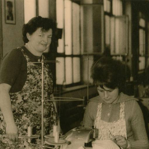 zwei Näherinnen in der Fabrik, eine sitzt an der Nähmaschine, eine steht